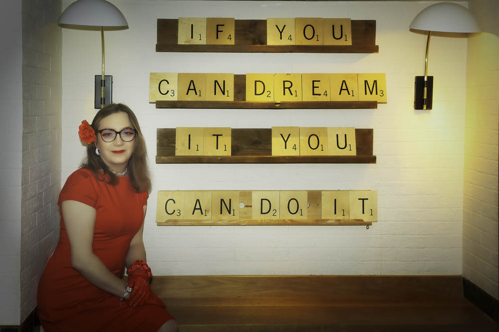 Annabelle in a red dress in front of a large Scrabble-tile sign reading 'If you can dream it you can do it'