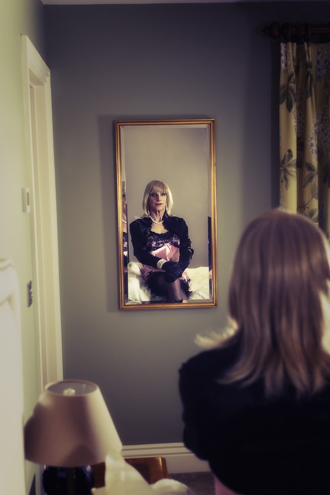 Daniella in a pink chemise, shot over the shoulder looking at her reflection in the mirror