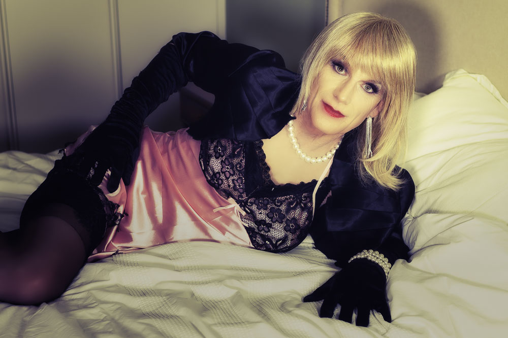 Daniella in a pink chemise lying on her side on white bedding