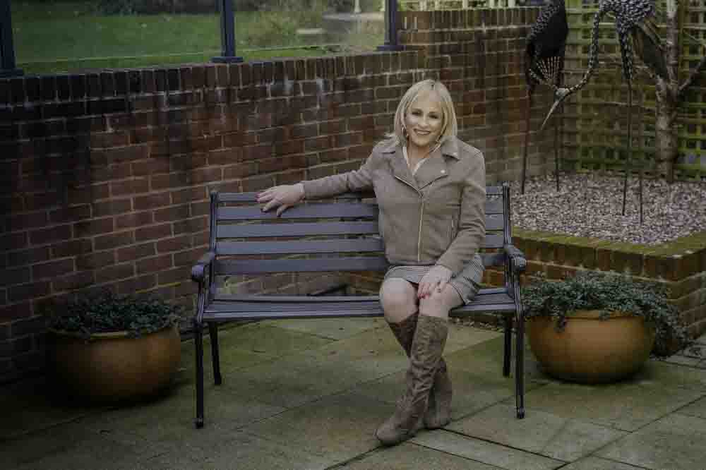 Stella in two piece skirt suit seated on bench outside