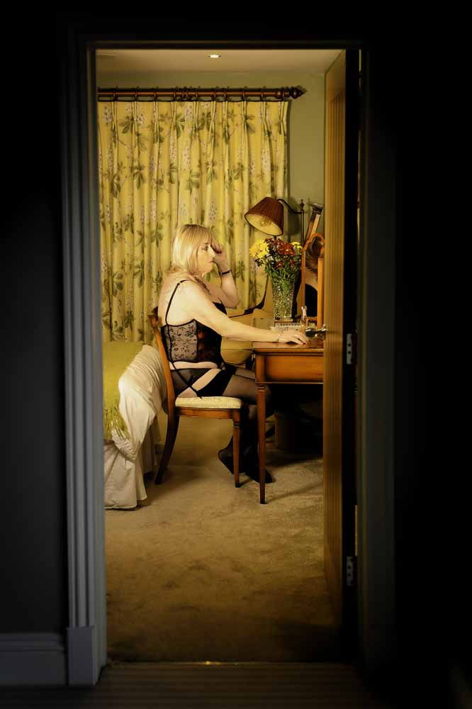 Stella viewed through doorway sitting at dressing table in lingerie