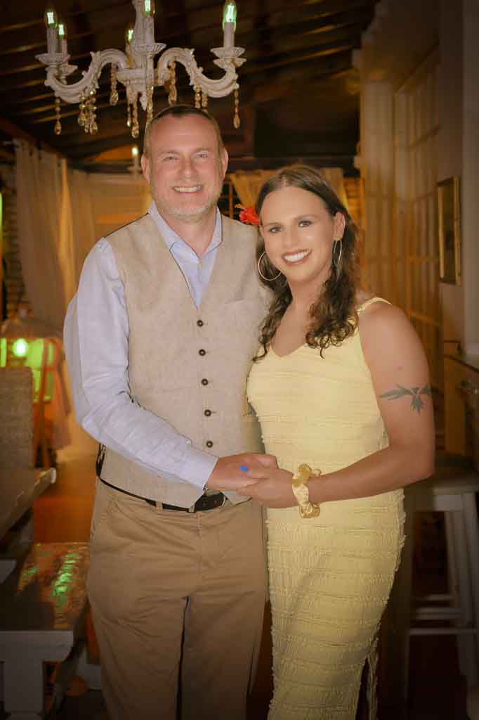 Evening photo of Jessica in a yellow sundress with Richard, who is wearing a cream waistcoat and light blue shirt, holding hands, Zakynthos