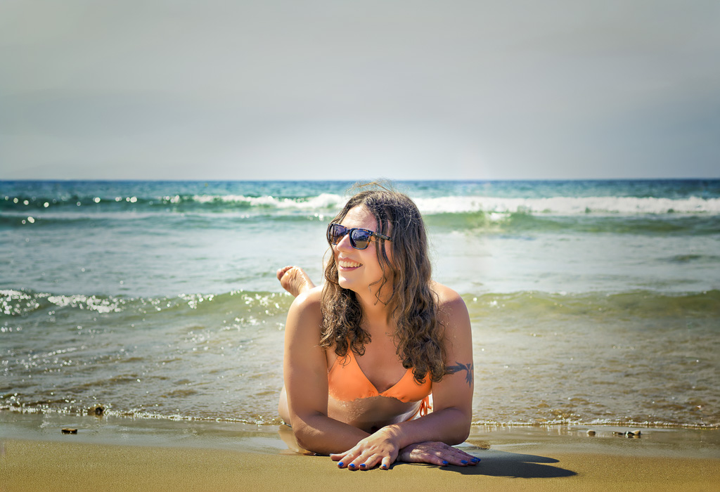 Jessica in an orange bikini, lying on her front on the beach as the sea laps around her legs, Gerakas Beach, Zakynthos