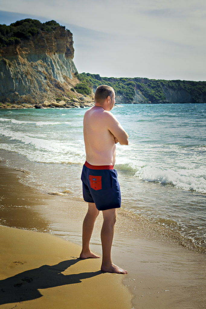 Richard in blue swim trunks on the beach, shot side-on, looking out to sea, Zakynthos