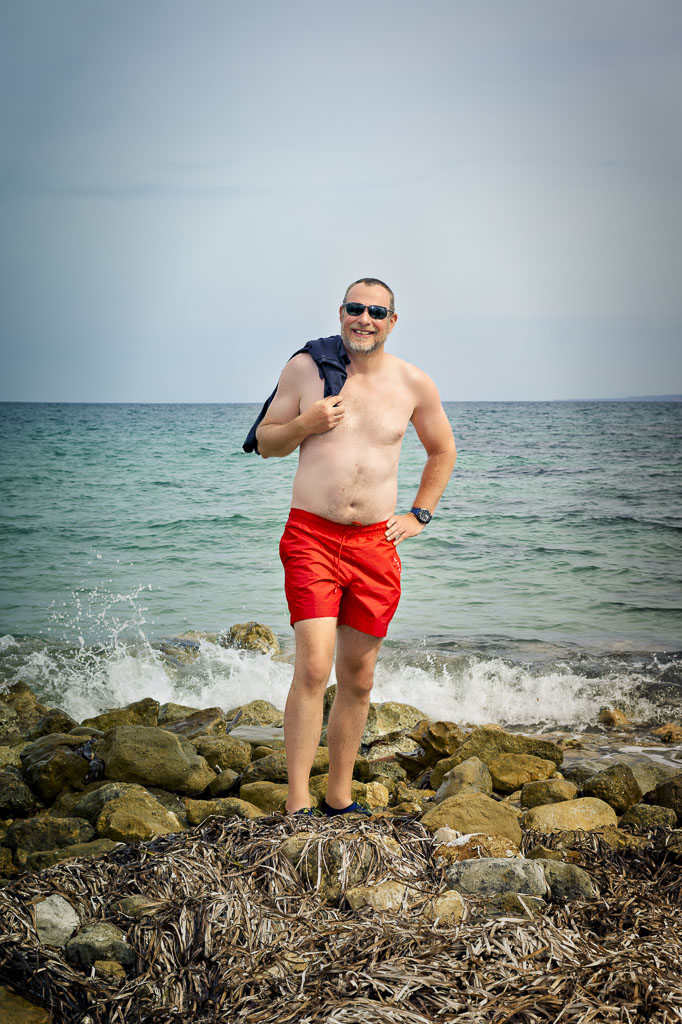 Richard in red swim trunks, standing on rocks, sea behind him, Zakynthos