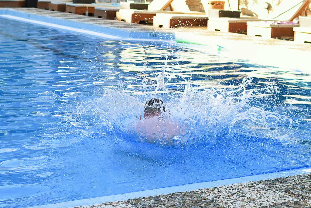 Richard in blue swim trunks, jumping into the pool with a big splash, photographed from behind, Zakynthos