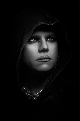 Moody black-and-white portrait of a model in a dark hood and chain necklace, looking upward
