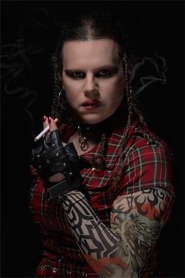 Punk-styled portrait in red tartan with a studded glove and tattoo sleeve, against a dark smoky background