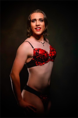 Model in red-and-black lace lingerie and a drop necklace, lit by warm low-key light